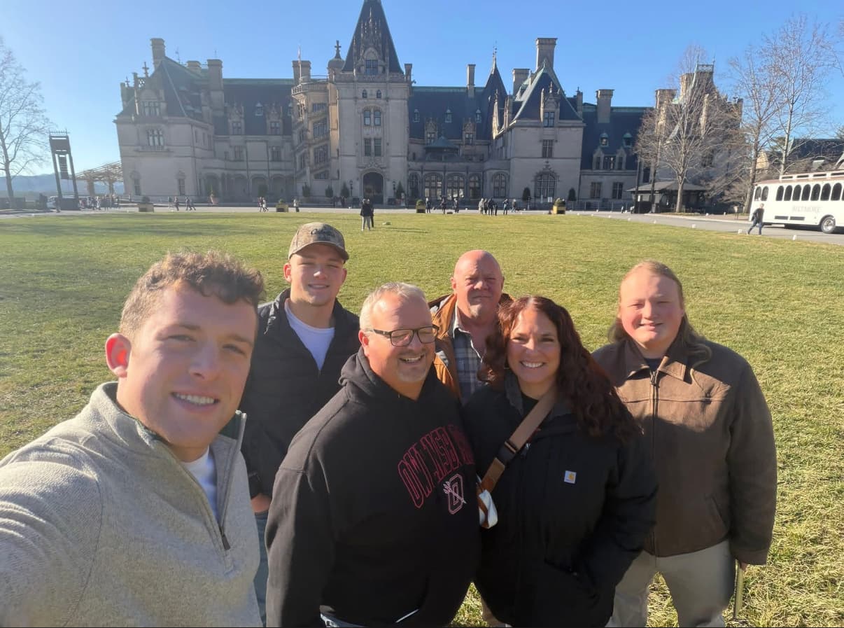 Group of six smiling people taking a selfie in front of the grand Biltmore Estate mansion.
